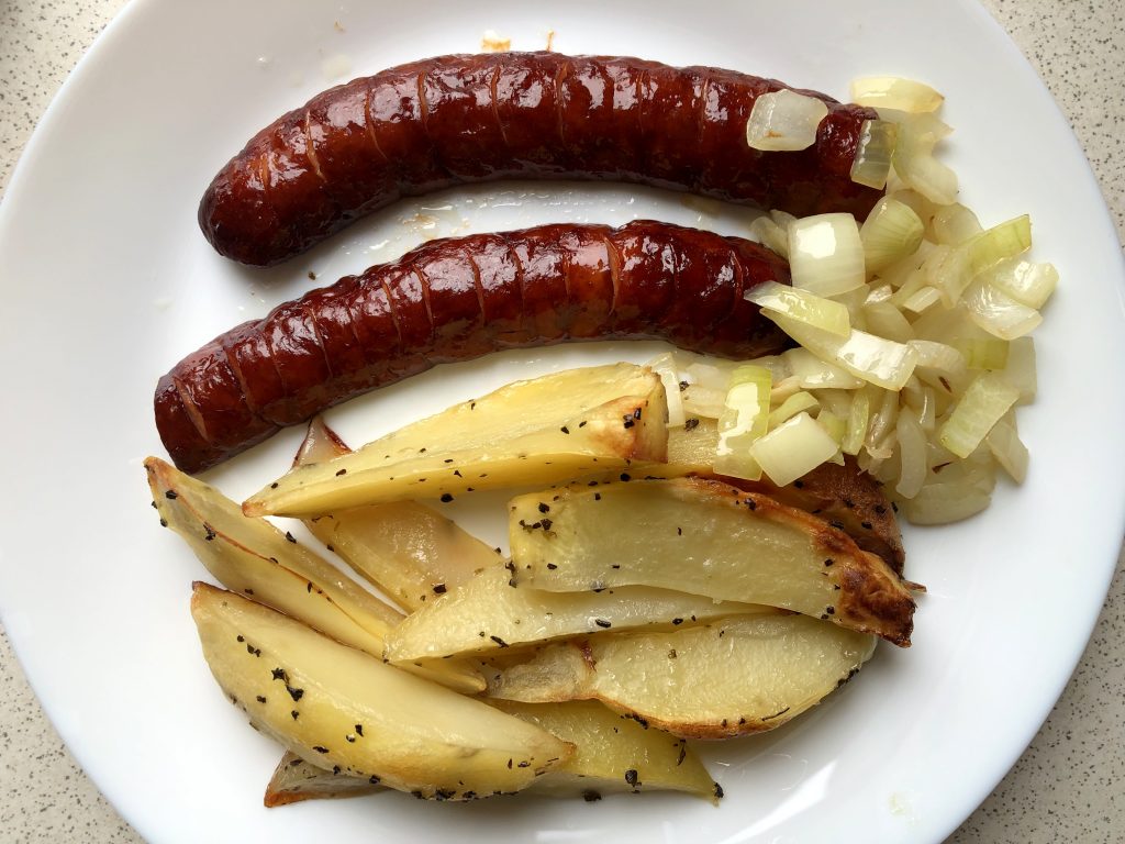 Polish baked sausage with onions and baked potatoes on the plate.