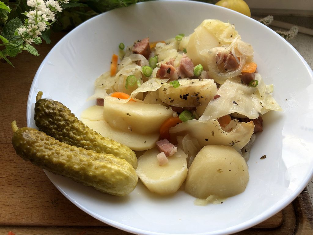 Polish farmer's casserole served on the plate with pickled cucumbers.